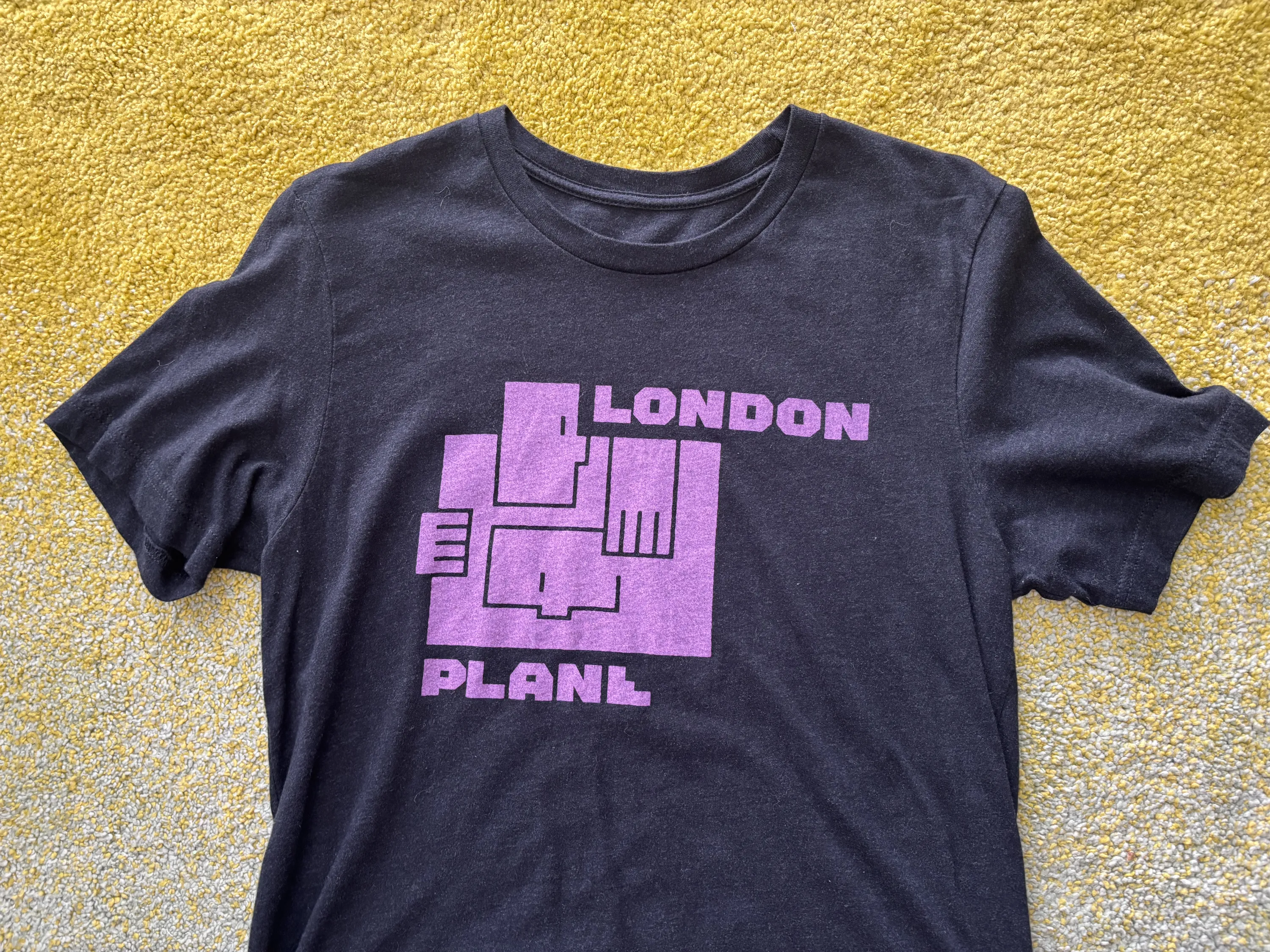 London Plane tee laying flat on yellow-to-teal gradient rug